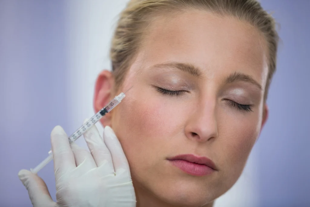 A close-up image of a woman with her eyes closed, receiving a Dysport injection on her cheek by a professional wearing white gloves, demonstrating the procedure's precision and care.