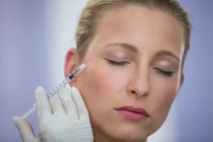 A close-up image of a woman with her eyes closed, receiving a Dysport injection on her cheek by a professional wearing white gloves, demonstrating the procedure's precision and care.