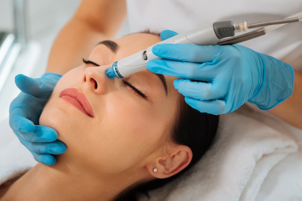 Woman receiving a professional Hydrafacial treatment with a handheld device, promoting deep cleansing, hydration, and glowing skin.